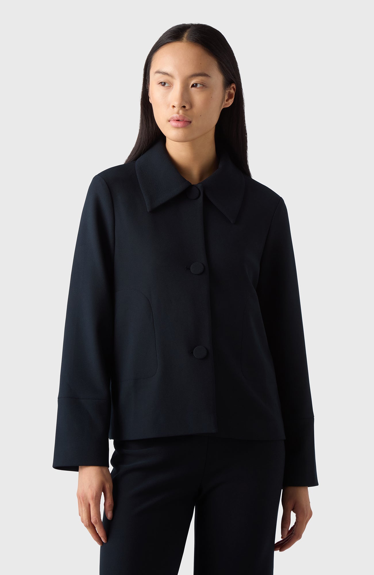 A woman wearing a navy Alba Crèpe Jacket with a classic collar, the jacket has long sleeves and is paired with black trousers.