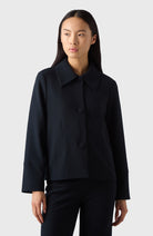 A woman wearing a navy Alba Crèpe Jacket with a classic collar, the jacket has long sleeves and is paired with black trousers.